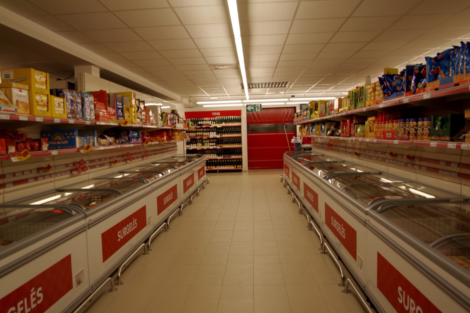 Un rayon de surgelés vide dans un supermarché, deux rangées de congélateurs ouverts sous des néons